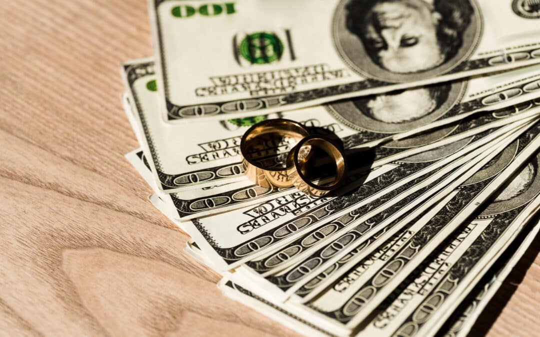 dollar banknotes near golden engagement rings on wooden surface